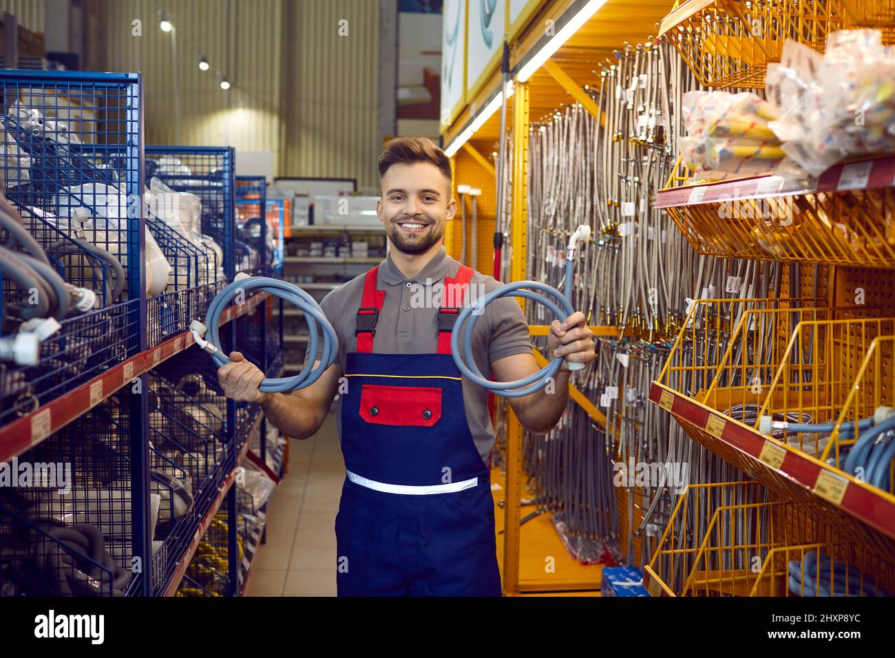 Un venditore felice al negozio di hardware che si trova nella corsia e mostra i tubi flessibili per la lavatrice Foto Stock