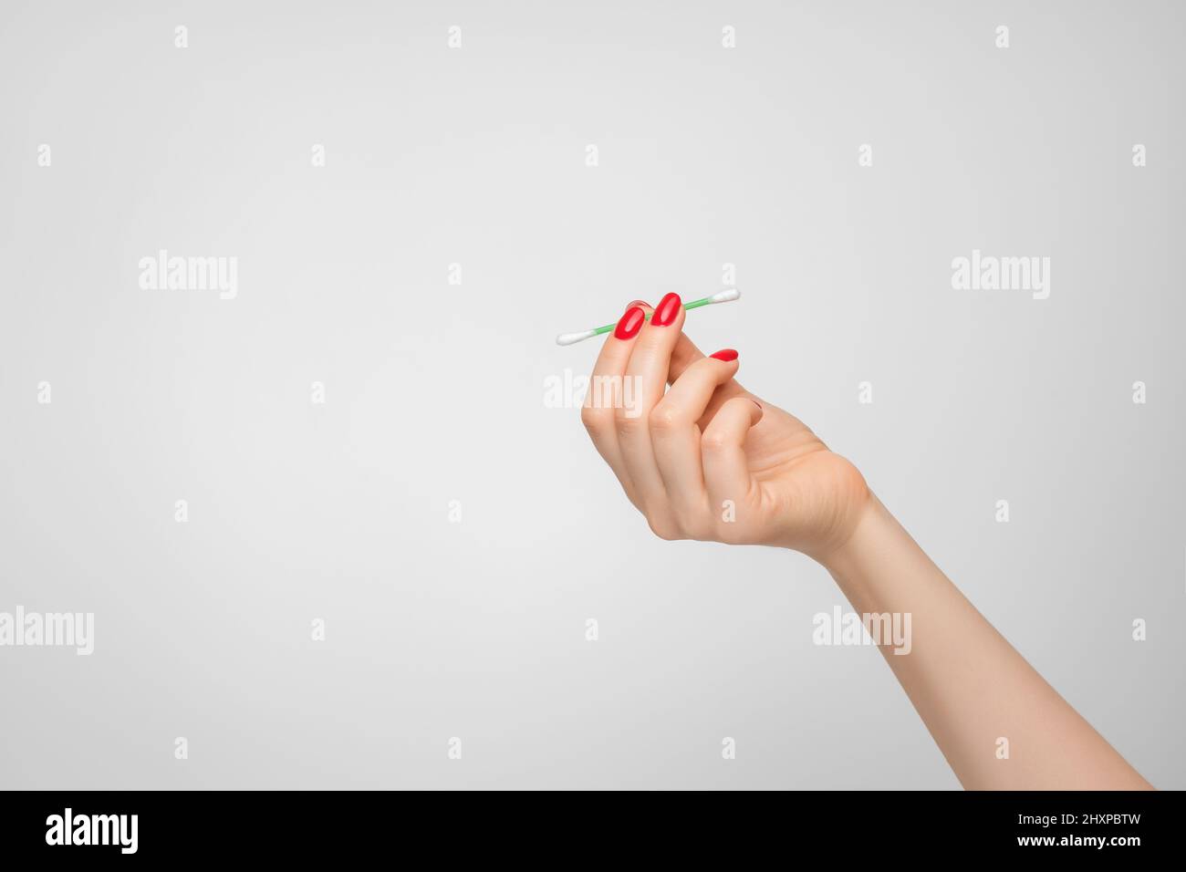 Un bastoncino di cotone per pulire le orecchie in mano di una donna con smalto rosso per unghie. Foto Stock