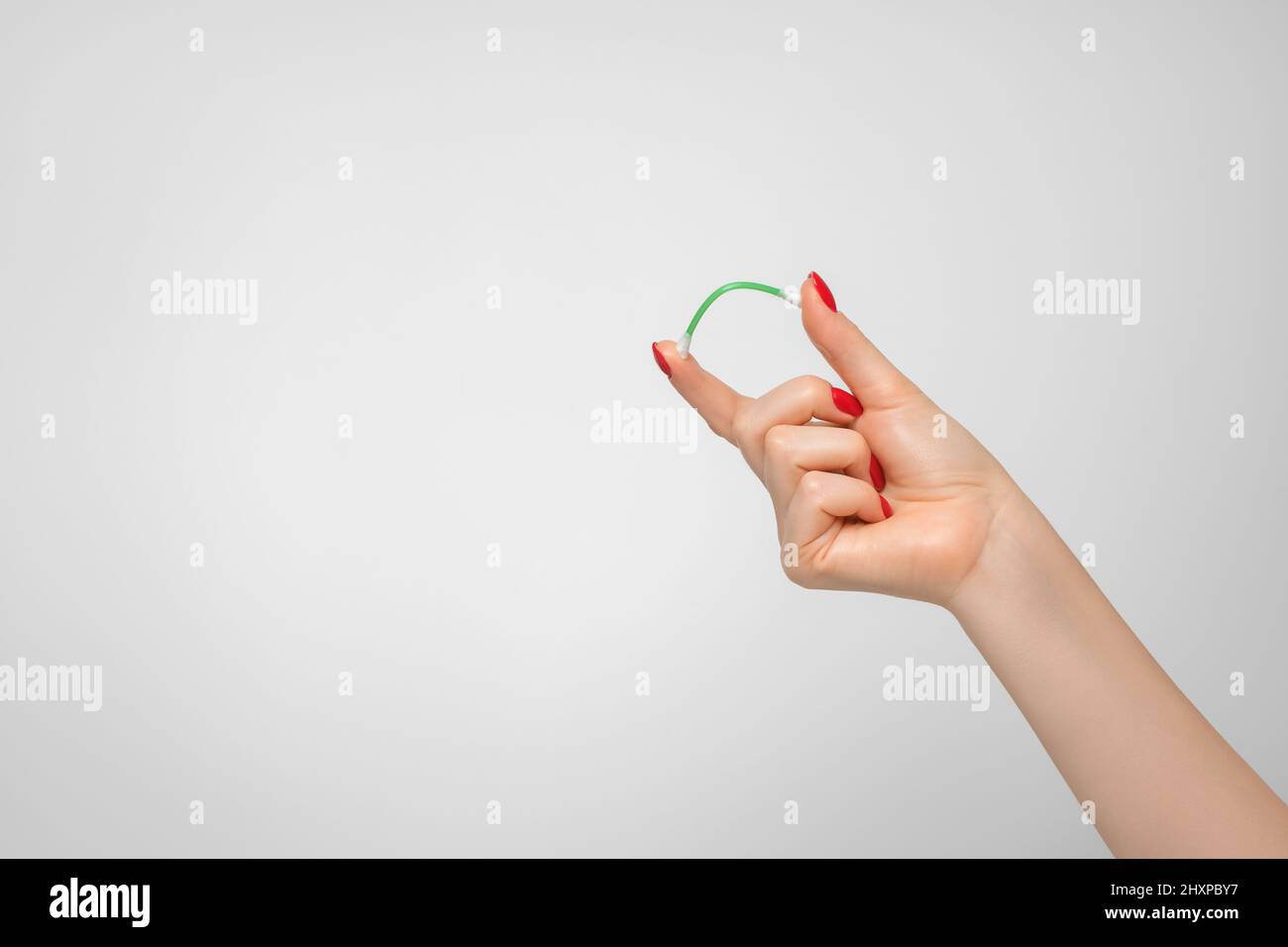 Un bastoncino di cotone per pulire le orecchie in mano di una donna con smalto rosso per unghie. Foto Stock