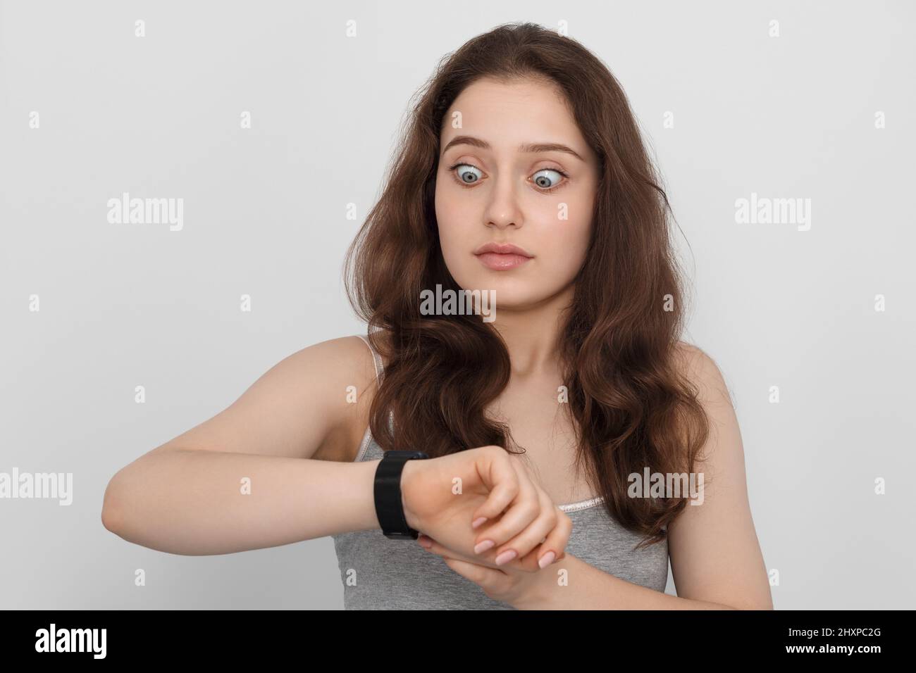 Una giovane ragazza con capelli lunghi guarda il suo orologio da polso in sorpresa Foto Stock