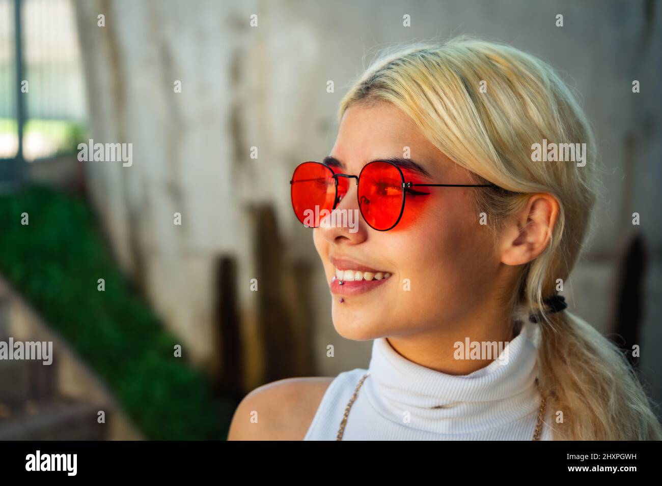 Primo piano di una bella giovane donna sorridente latina che indossa una maglietta bianca e occhiali da sole rossi. Concetto di gioia. Foto Stock
