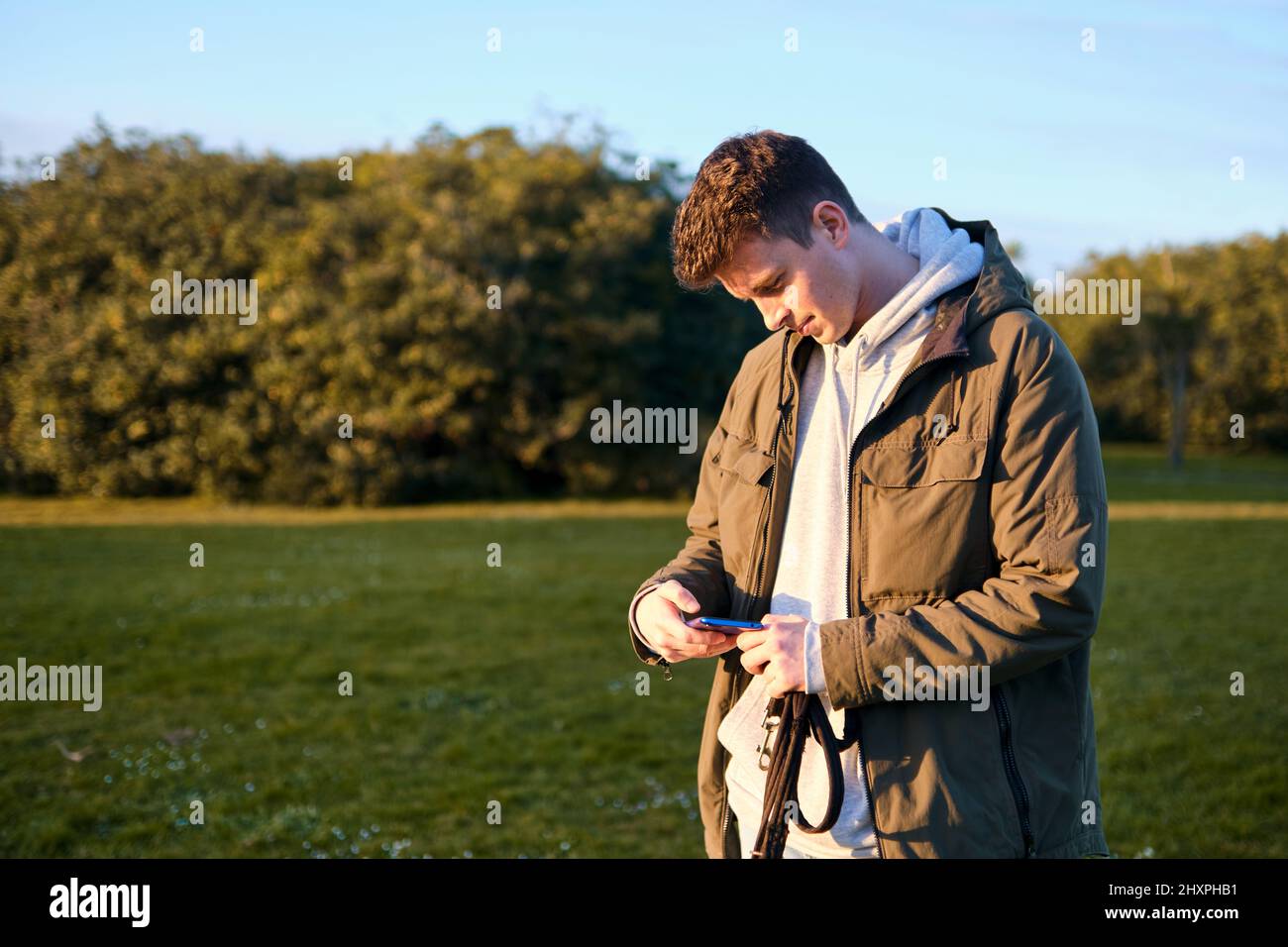 Giovane biondo che guarda con interesse e stranezza allo schermo del suo cellulare in un parco Foto Stock