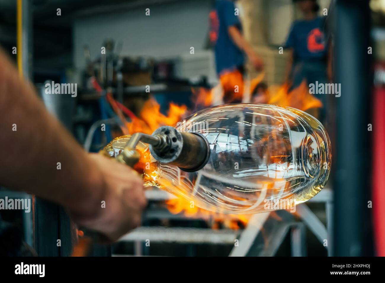 Primo piano di un artigiano soffiatore di vetro che forma il vetro fuso caldo a fuoco forte all'interno di un'officina. Lavorazione manuale del vetro da parte degli artigiani all'interno di un gla Foto Stock