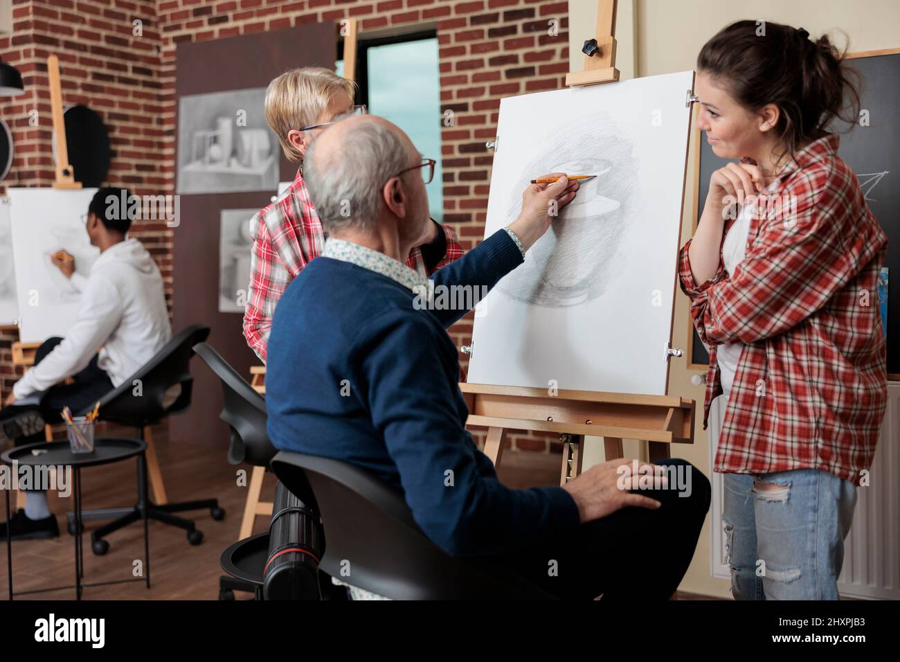 L'insegnante supervisiona lo studente anziano mentre disegna il modello di vaso su tela che lavora alla tecnica di illustrazione nello studio di creatività. Un team diversificato che attenta la classe artistica sviluppando abilità artistiche Foto Stock