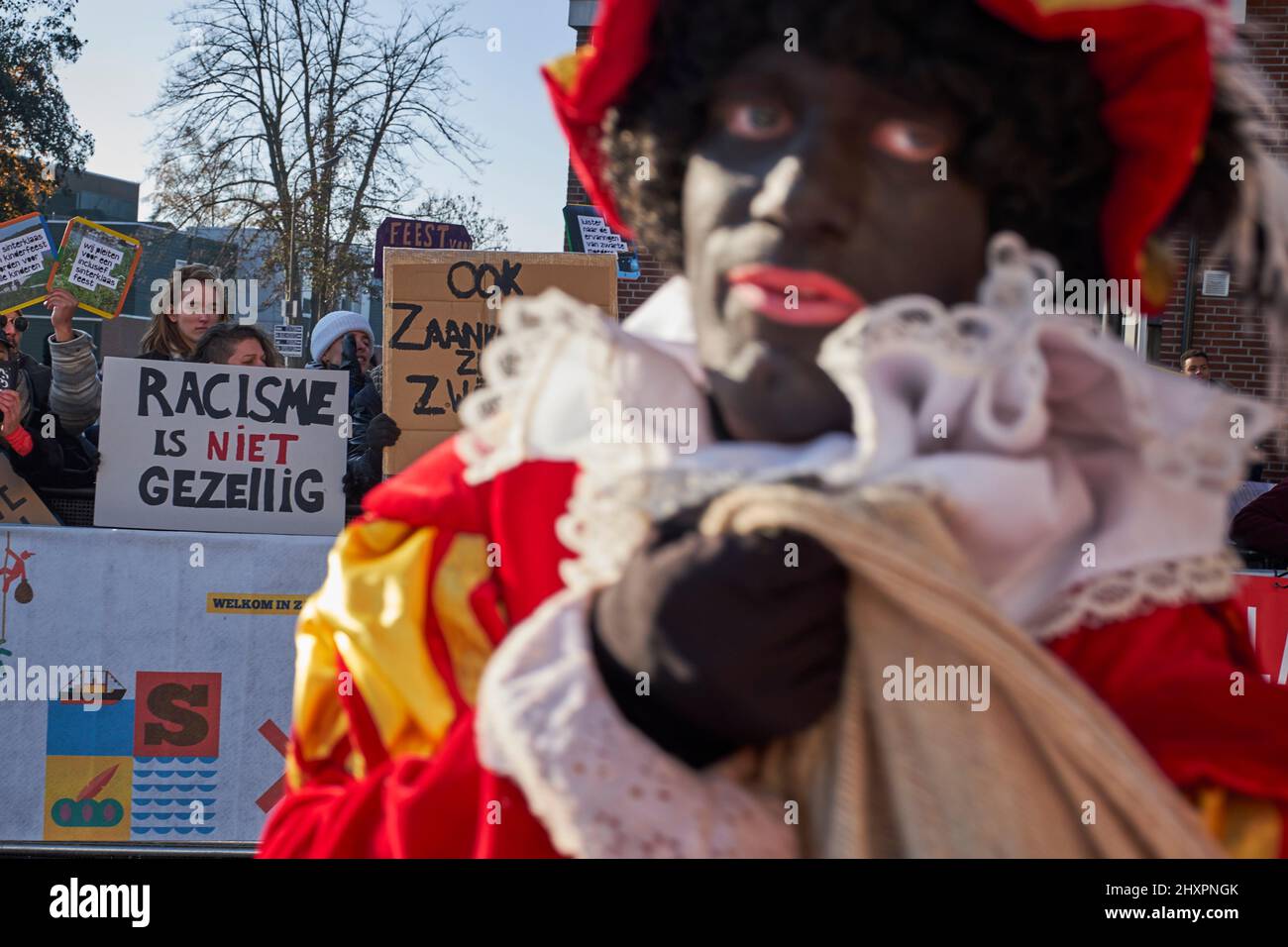 Molte persone travestite da Zwarte Piet passano di fronte alla dimostrazione del gruppo anti-razzista a Zaandam Foto Stock