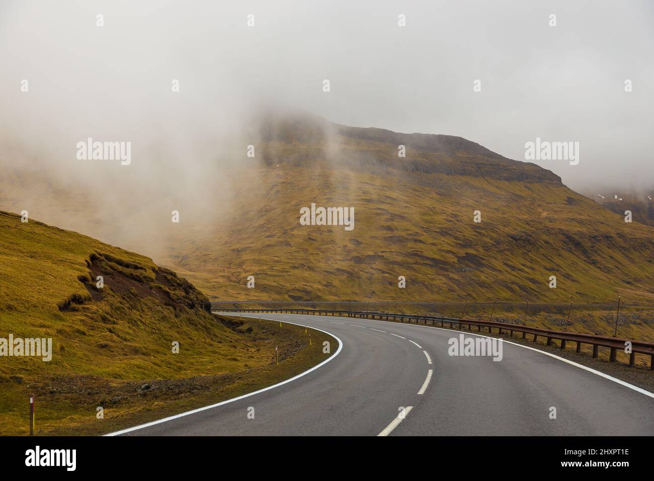 Strada asfaltata lungo le colline dell'isola di Streymoy. Nuvole spesse nella valle. Isole Faroe, Danimarca. Foto Stock