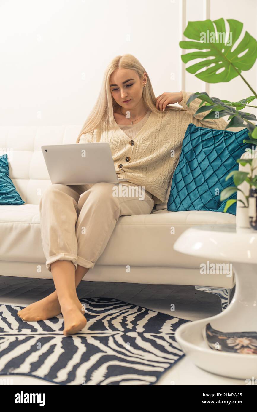 Giovane bella bionda caucasica donna seduta sul divano guardando il portatile remoto lavoro full shot . Foto di alta qualità Foto Stock