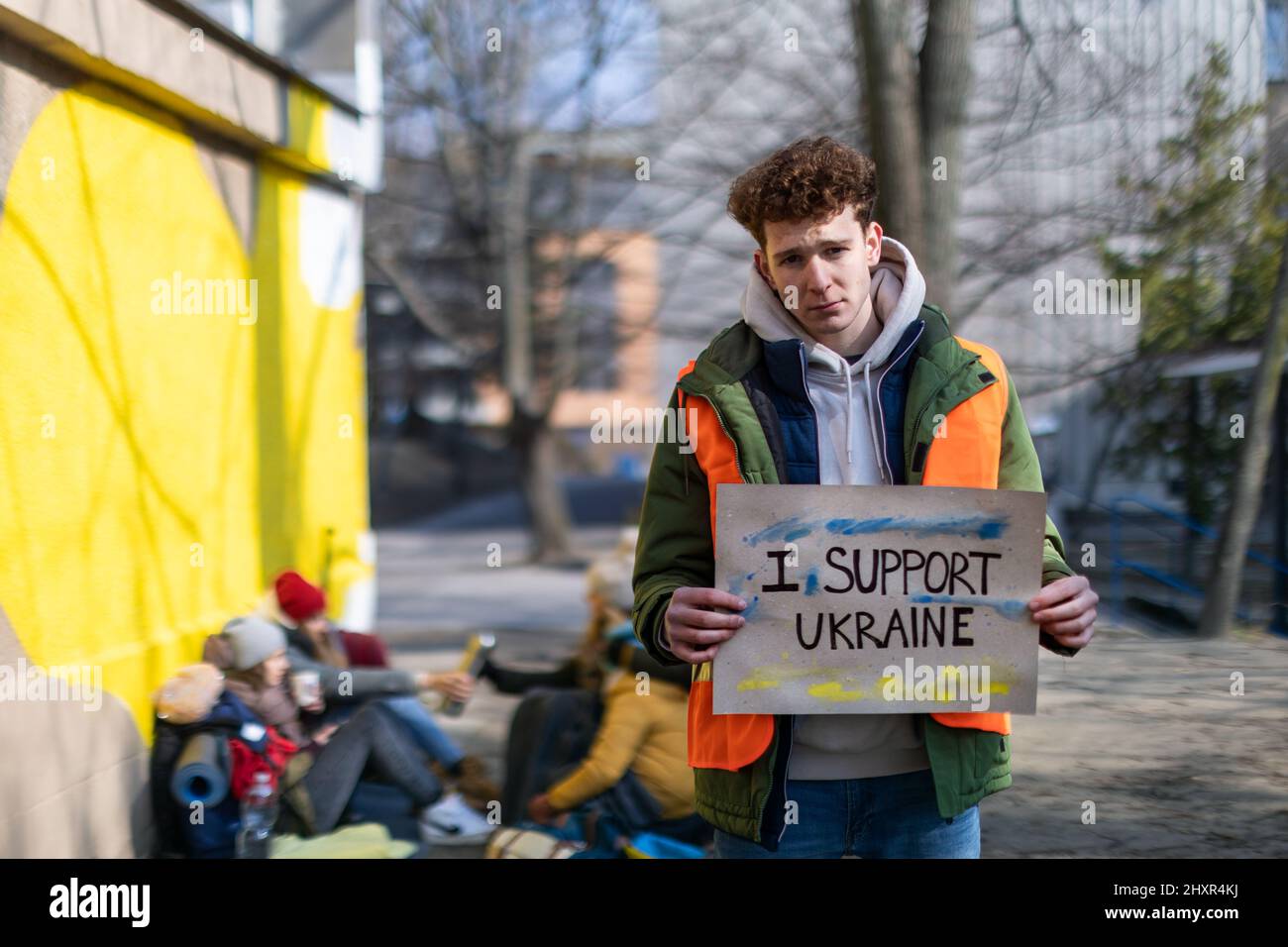 Protesta contro l'invasione russa dell'Ucraina. Uomo volontario che tiene bandiera anti guerra vicino al campo di rifugiati. Foto Stock