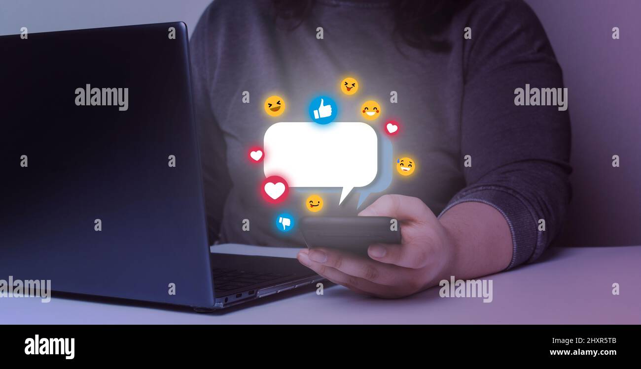 Giovane donna che invia messaggi di testo con il suo smartphone. Ologramma emoji con schermo tattile mobile. Foto Stock