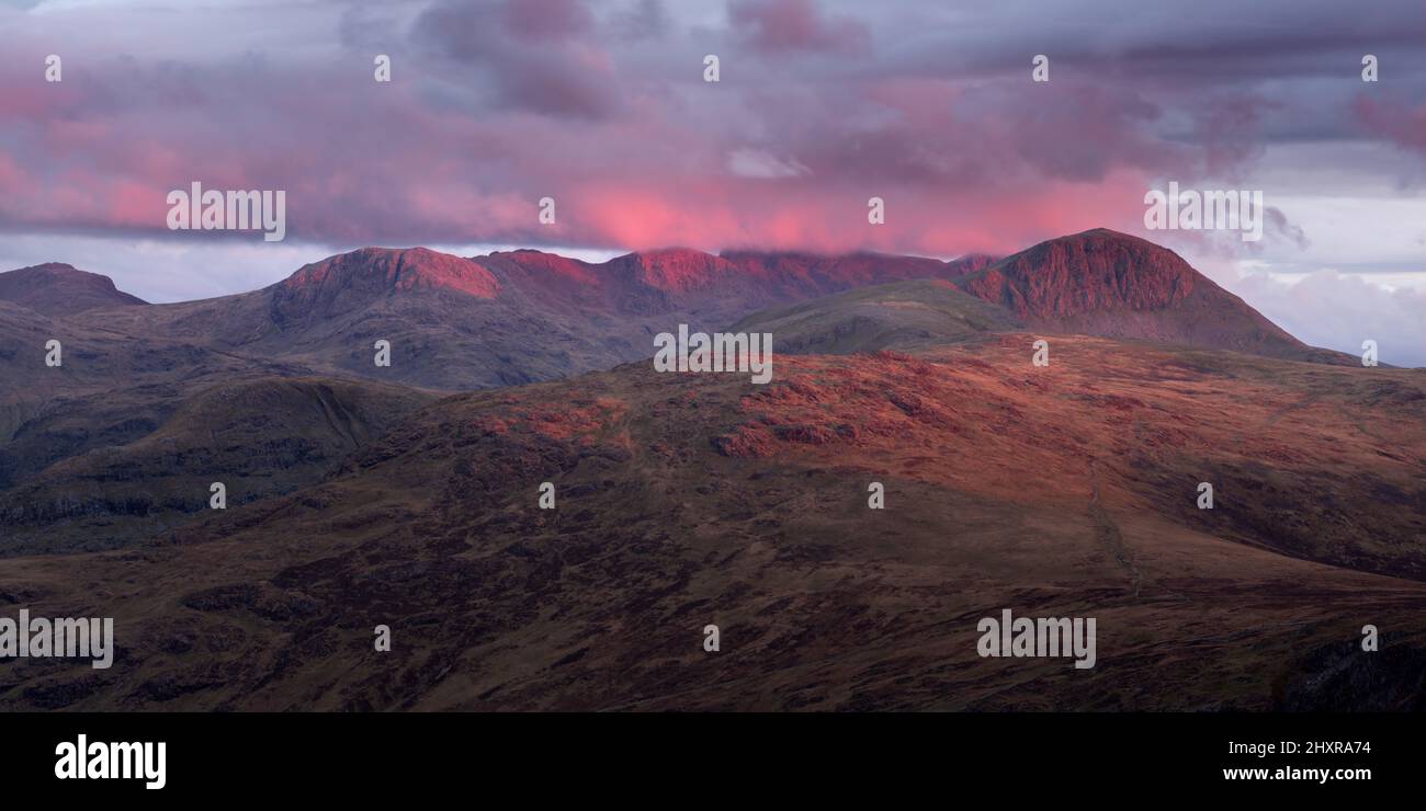 Vista panoramica dell'aspra catena montuosa del Lake District con luce solare rossa che colpisce la catena montuosa Scafell; la montagna più alta dell'Inghilterra. Foto Stock