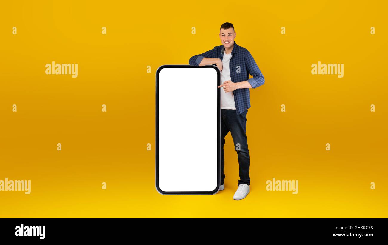 Happy Man che mostra schermo telefono enorme puntando le dita, sfondo giallo Foto Stock
