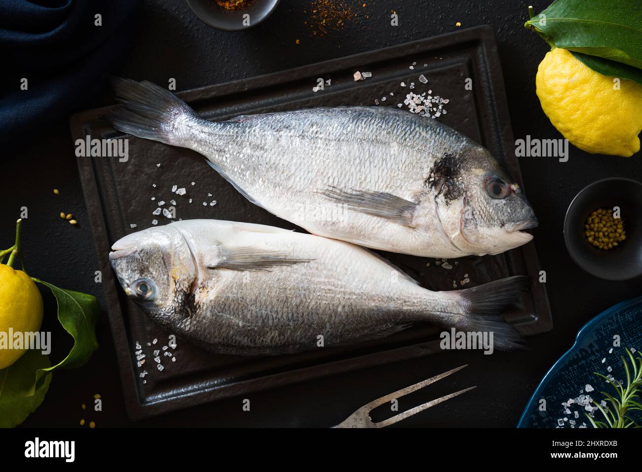 Orata a testa dorata su un tagliere nero e altri ingredienti, pronti per la cottura Foto Stock