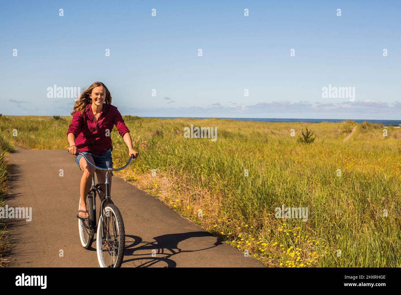 Una giovane donna corre una bicicletta da mare su un sentiero lastricato. Foto Stock