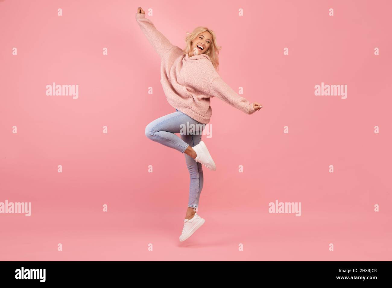 Gioiosa giovane donna che salta, che si diverte e sorride, che è di buon umore e che si gira intorno su sfondo rosa Foto Stock