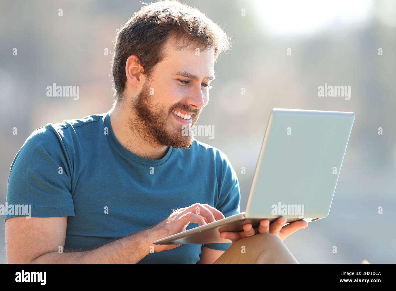 Uomo felice che usa il laptop che guarda i contenuti multimediali seduti in natura Foto Stock
