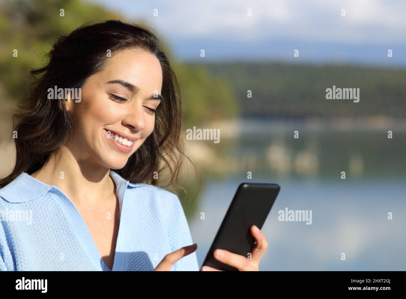 Donna felice utilizzando smartphone in piedi in un bel lago Foto Stock
