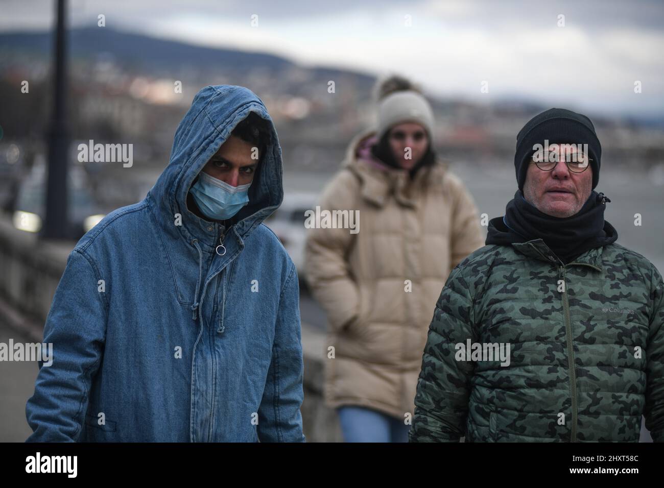 Persone che indossano maschere per il viso e abiti invernali sulla riva del Danubio, Budapest, Ungheria Foto Stock