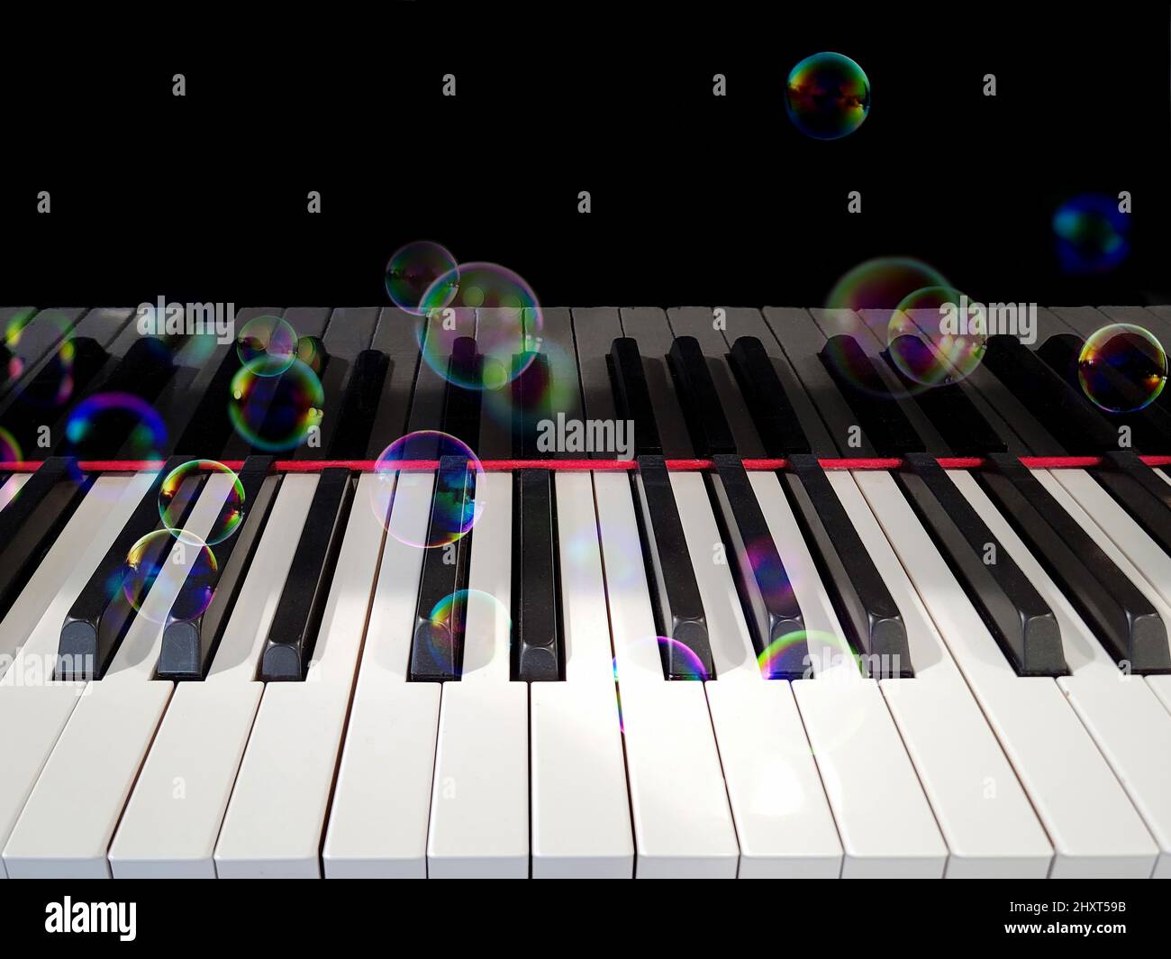 Bolle iridescenti fluttuanti su una tastiera a piano Foto Stock