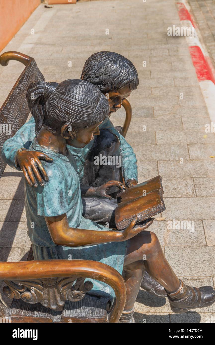 Foto verticale di un monumento in bronzo di un ragazzo e una ragazza che legge sulla panchina in Thailandia Foto Stock