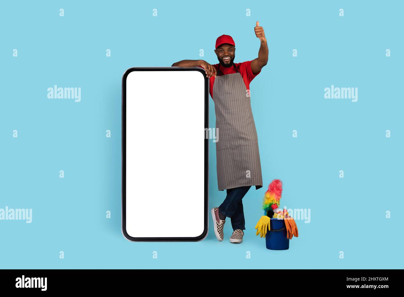 Black Cleaner Man in piedi vicino a smartphone Big Blank e mostrando Thumb in alto Foto Stock