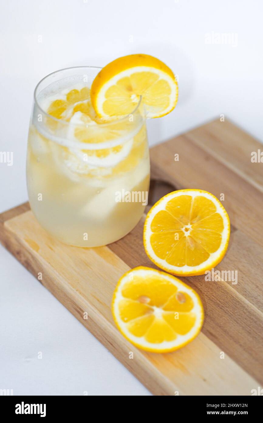 Rinfrescante succo di limone e due metà di limone sul vassoio di legno sulla superficie bianca Foto Stock