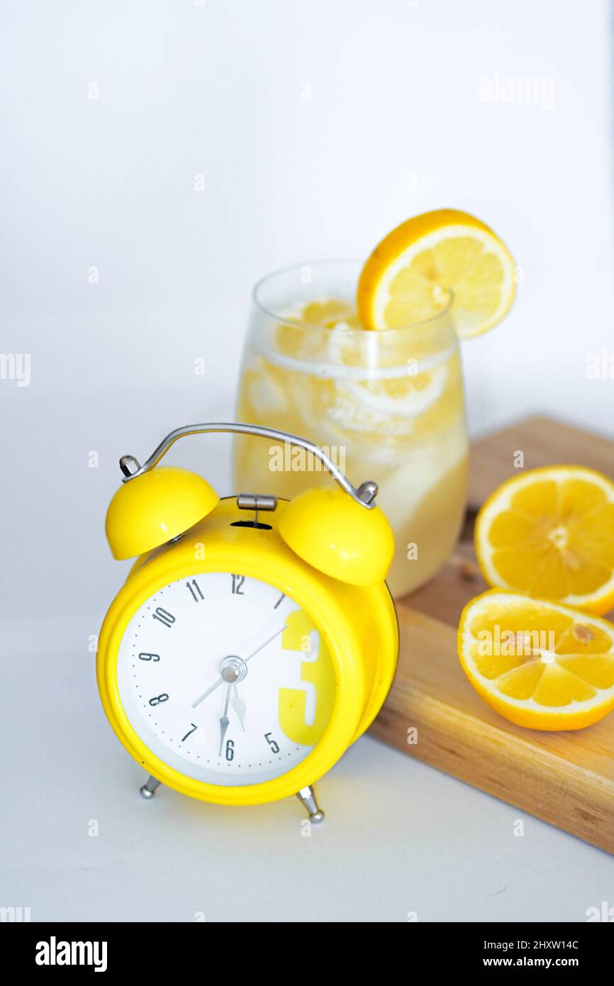 Rinfrescante succo di limone, due metà di limone e un orologio sul vassoio di legno su una superficie bianca Foto Stock
