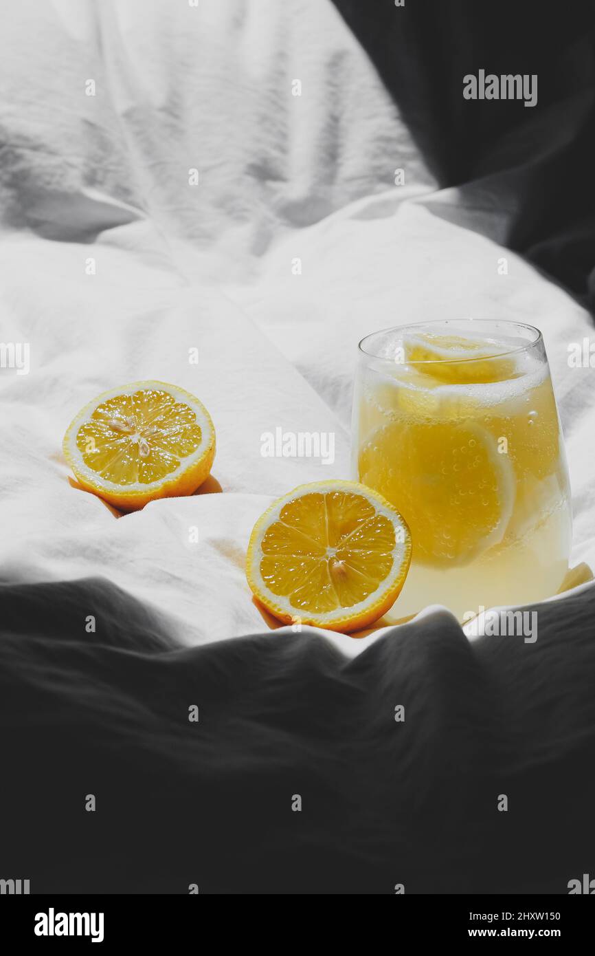 Rinfrescante succo di limone e due metà di limone sulla coperta bianca sotto la luce del sole Foto Stock