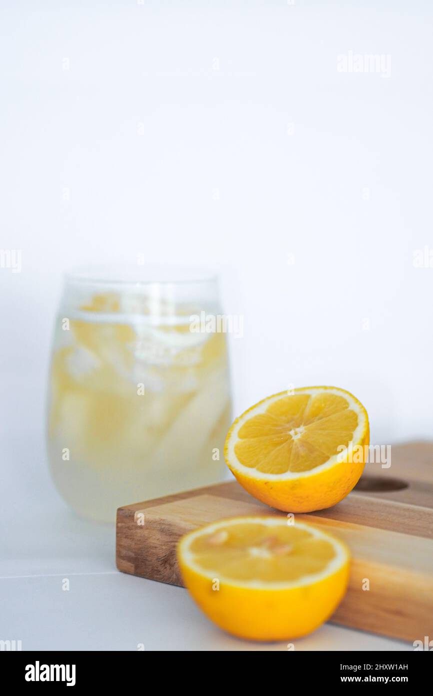 Rinfrescante succo di limone e due metà di limone sul vassoio di legno sulla superficie bianca Foto Stock