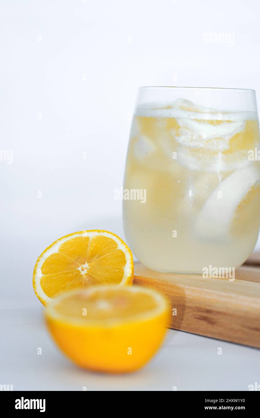 Rinfrescante succo di limone e due metà di limone sul vassoio di legno sulla superficie bianca Foto Stock