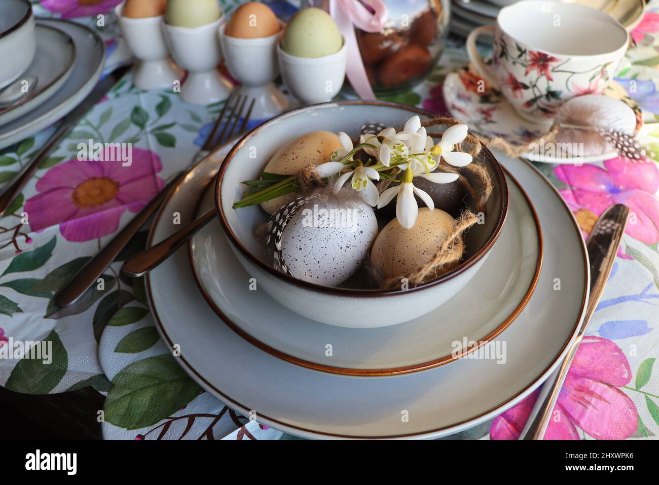 Elegante tavolo di Pasqua con uovo in ciotola sul tavolo. Moderno uovo di pasqua naturale tinto, fiori su piatto e posate. Pasqua festive decorazioni tavola Foto Stock