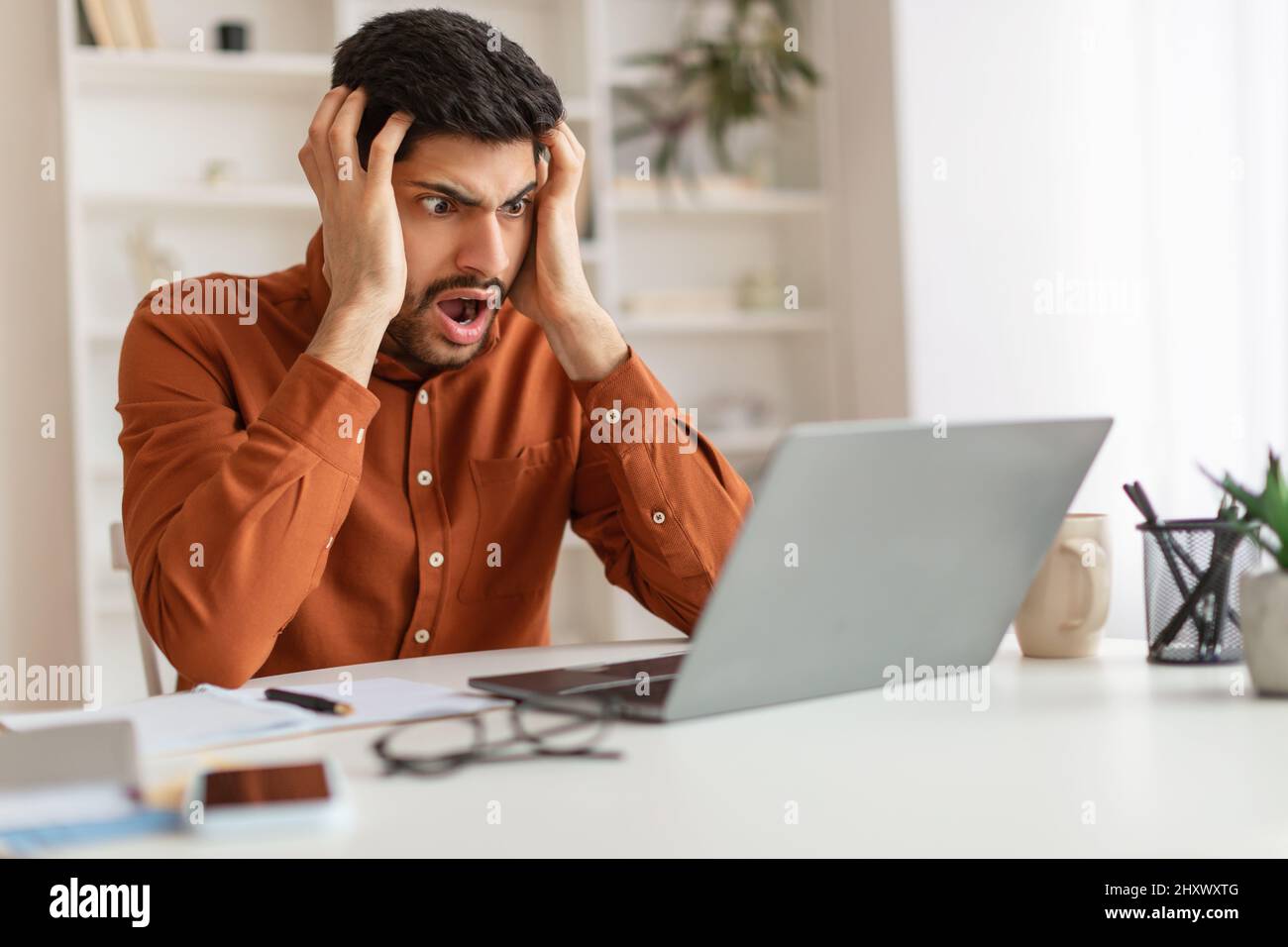 Scioccato ragazzo arabo afferrare la testa utilizzando il portatile Foto Stock