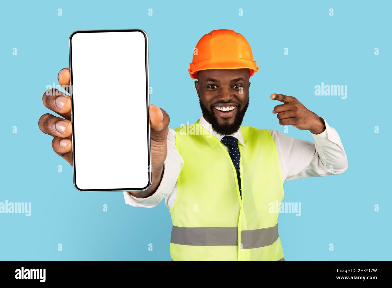 Happy African American Construction Worker che punta allo smartphone vuoto in mano Foto Stock
