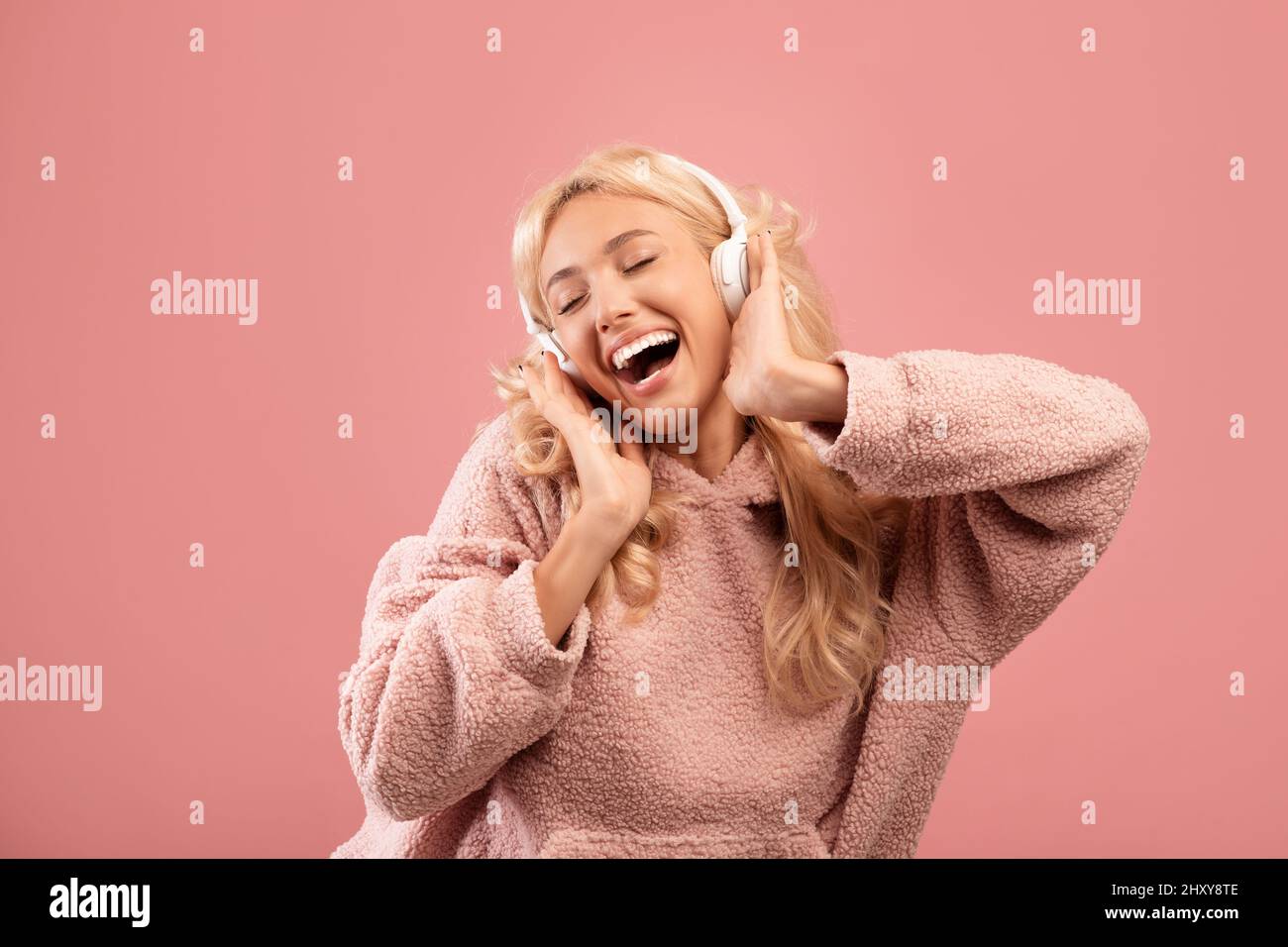 Cuffia stereo di ultima generazione. Una donna entusiasta di ascoltare la playlist con gli occhi chiusi in cuffie wireless, sfondo rosa Foto Stock