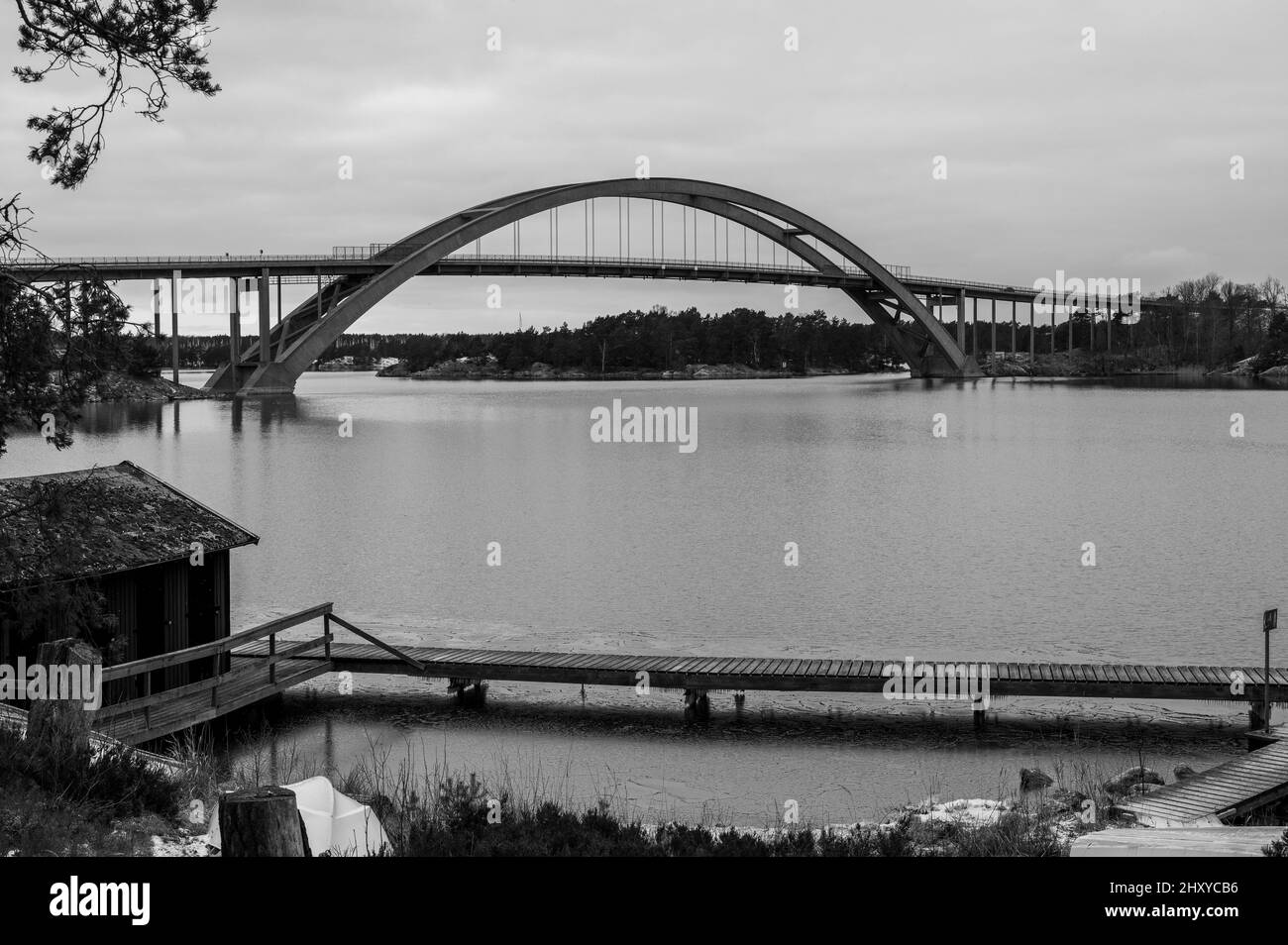Una bella foto di un vecchio molo di legno vicino ad un lago con un ponte sullo sfondo - in scala di grigi Foto Stock