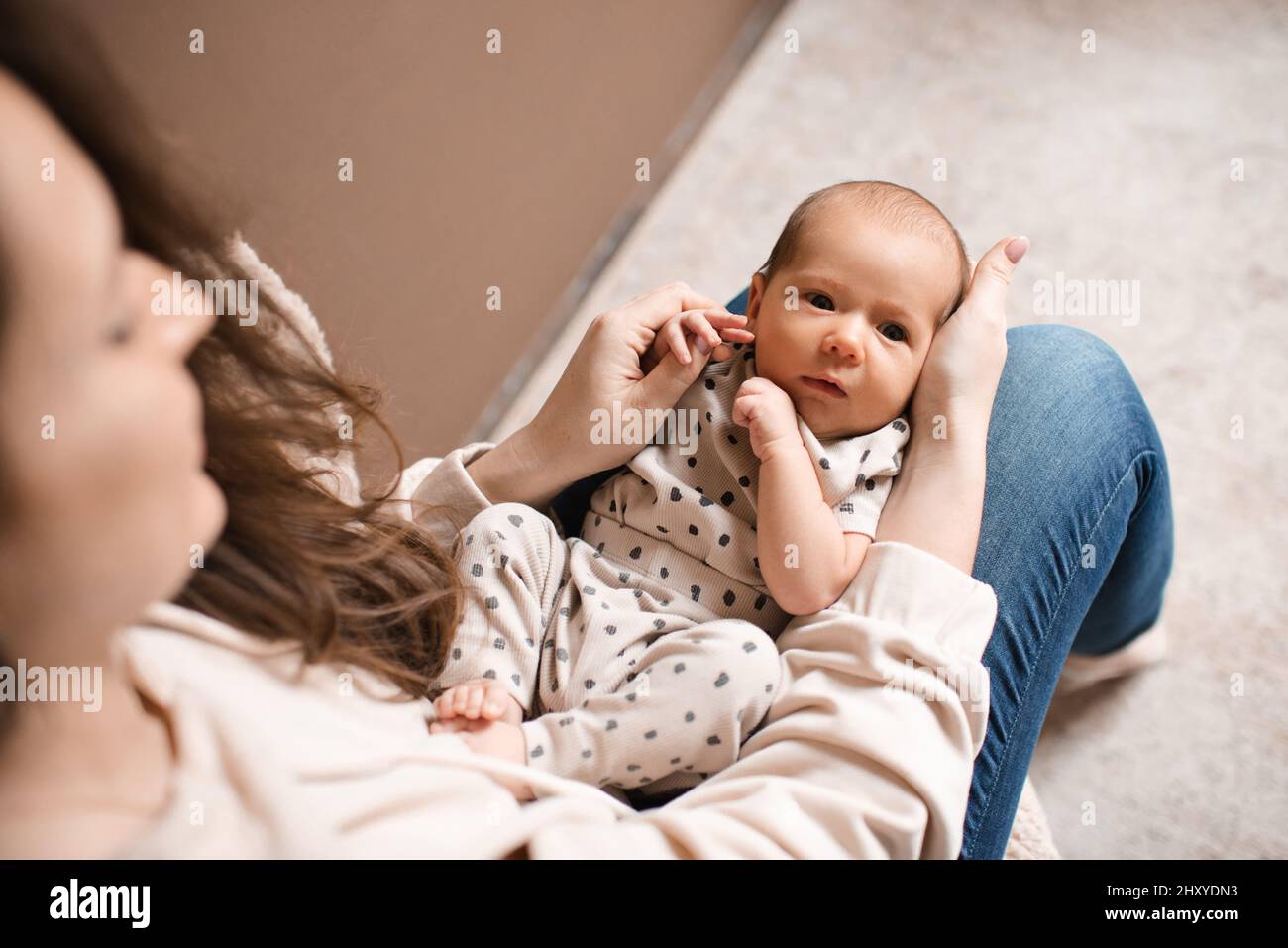 Madre giovane che tiene il bambino neonato sdraiato sulle mani nella stanza a casa. Concetto di stile di vita familiare. Maternità. Foto Stock