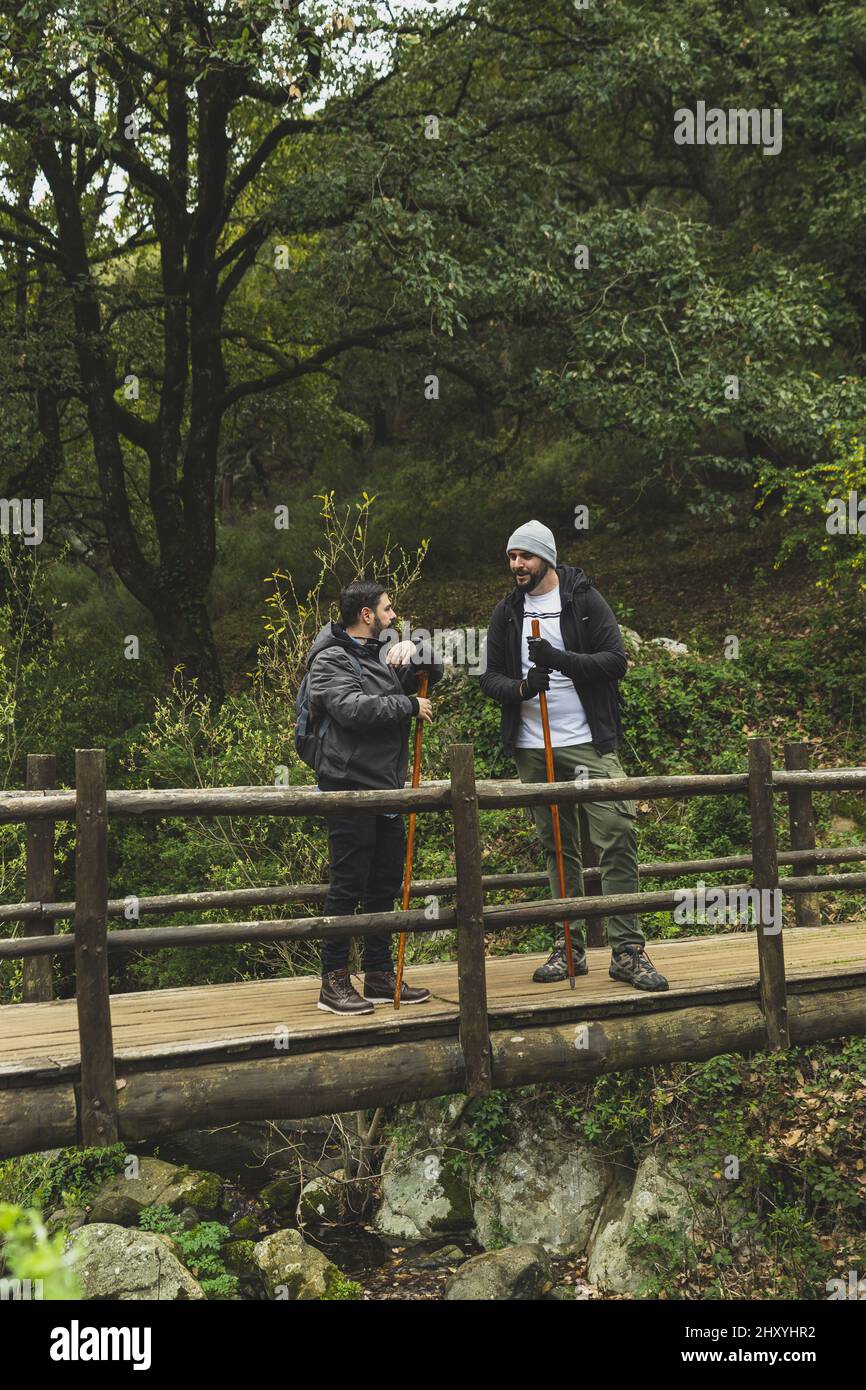 Colpo verticale di due uomini con bastoncini da trekking in piedi su un ponte di legno in una foresta Foto Stock