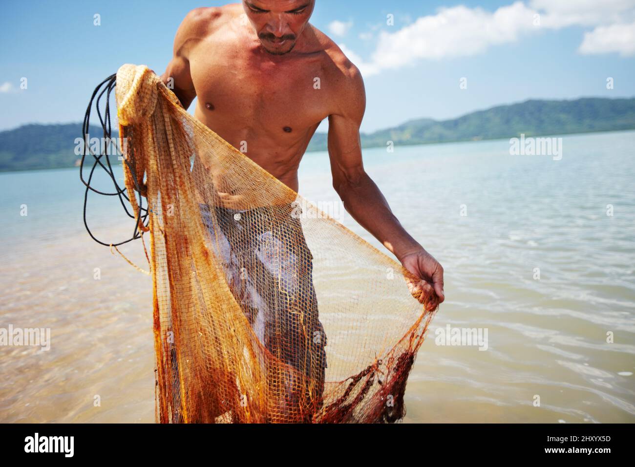 Solo facendo il suo lavoro. Shot di un tradizionale pescatore tailandese in piedi in acqua tenendo una rete. Foto Stock