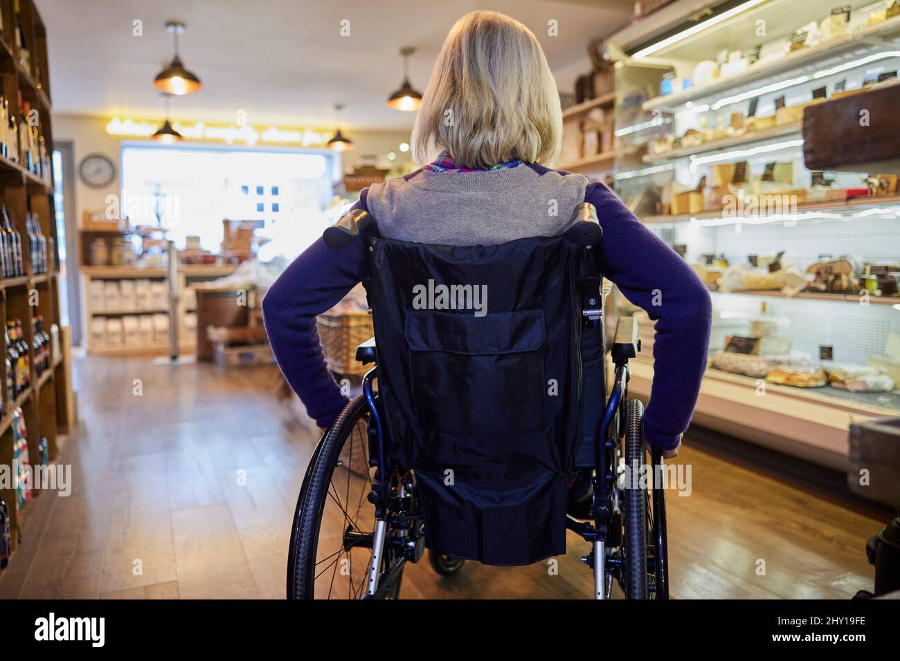 Vista posteriore della donna in Wheelchair Shopping for Food a Delicatessen Foto Stock