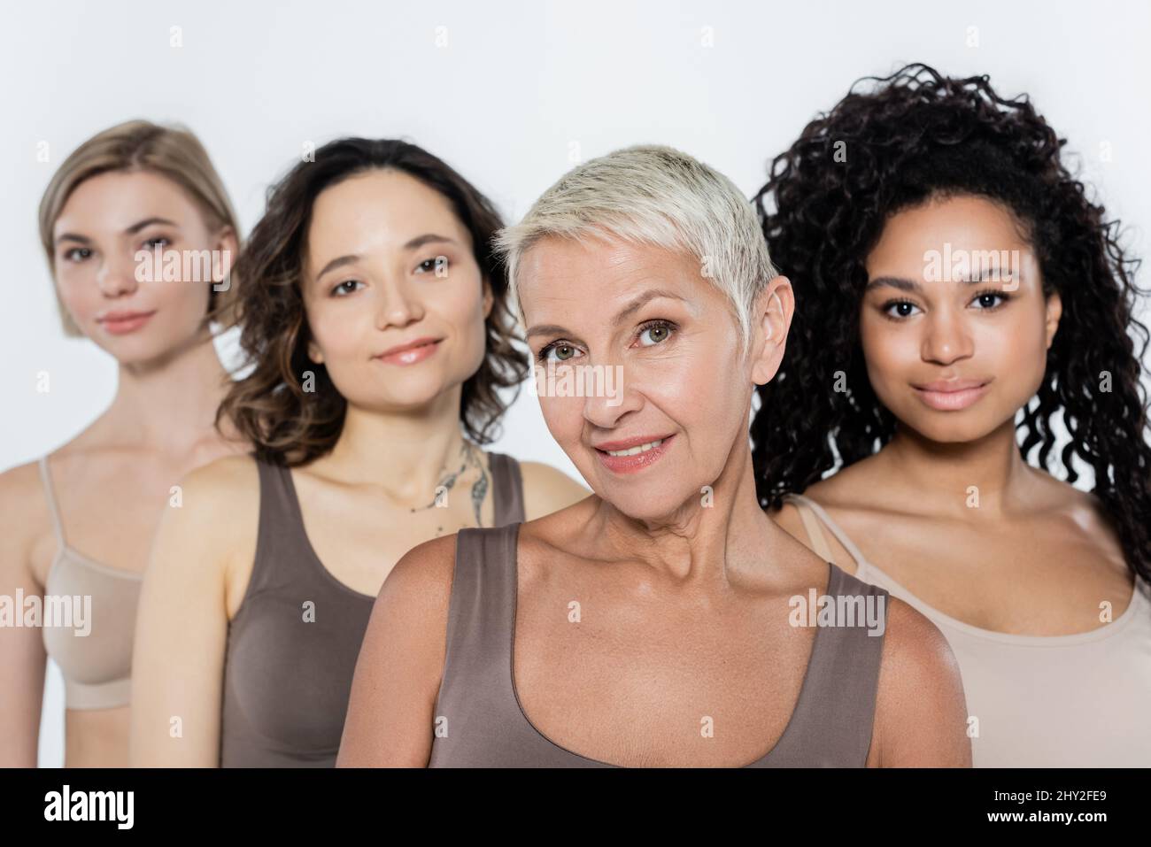 Donna anziana dai capelli grigi sorridente alla macchina fotografica vicino agli amici interracial blurred isolati su grigio,immagine di scorta Foto Stock