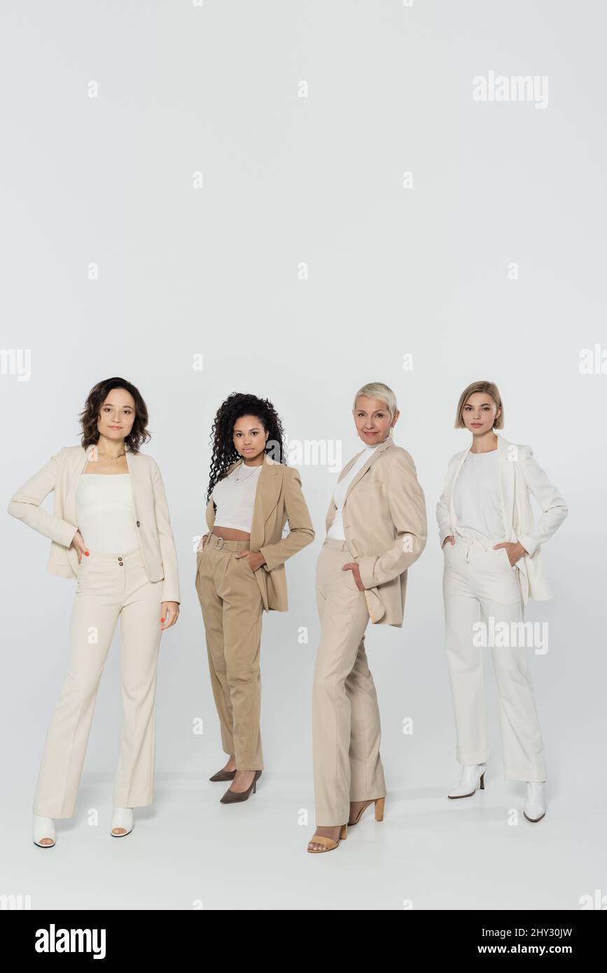 Tutta la lunghezza di donne d'affari sorridenti che posano su sfondo grigio, concetto di femminismo, immagine di stock Foto Stock