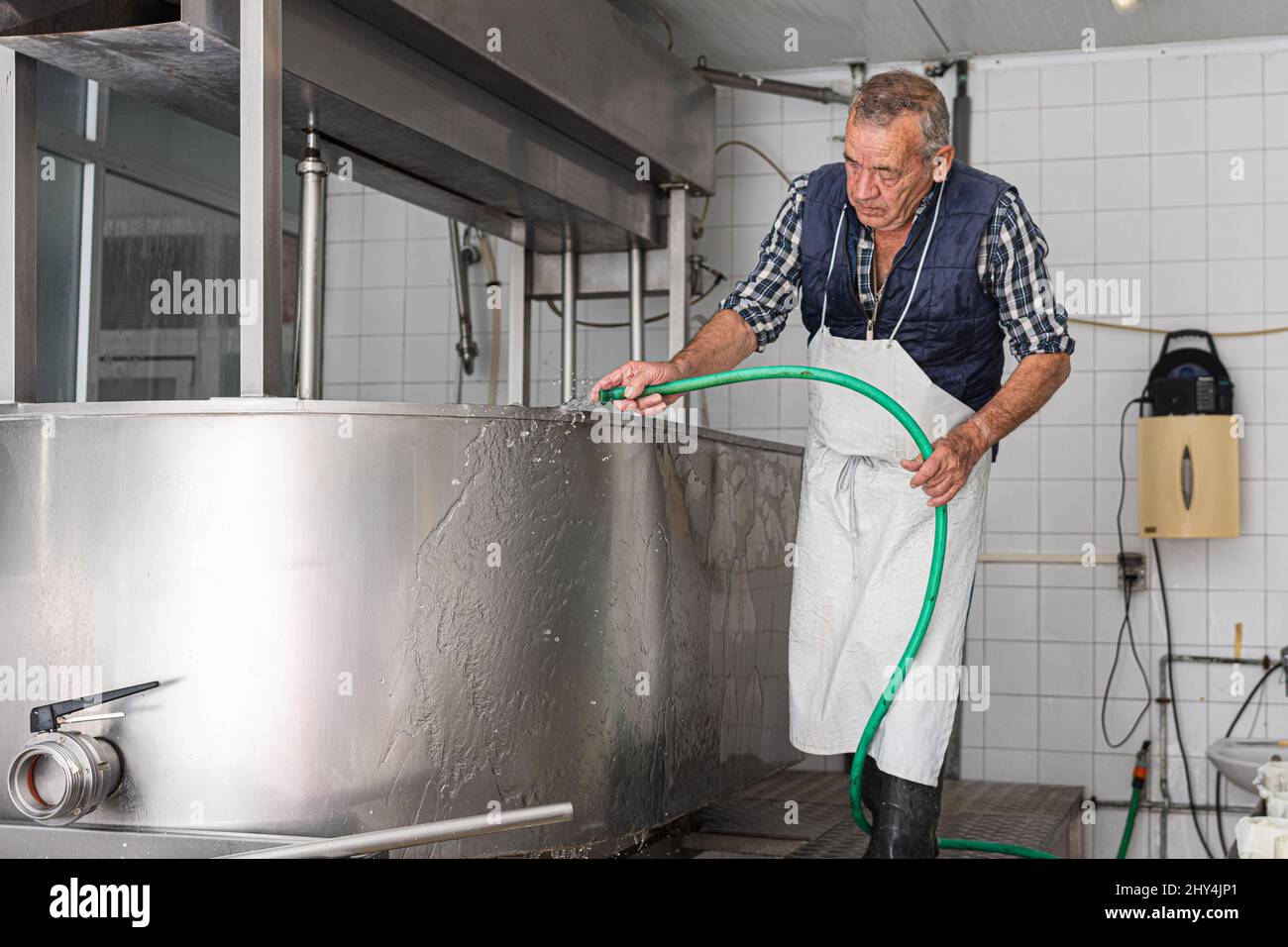 uomo anziano in un grembiule risciacquare il sapone da un contenitore di acciaio inossidabile Foto Stock