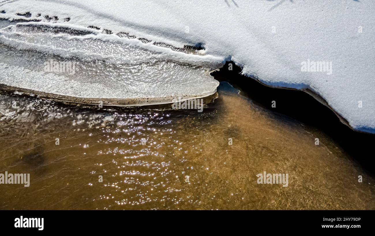 Un piccolo ruscello con ghiaccio e neve che si scioglie creando acqua in movimento Foto Stock