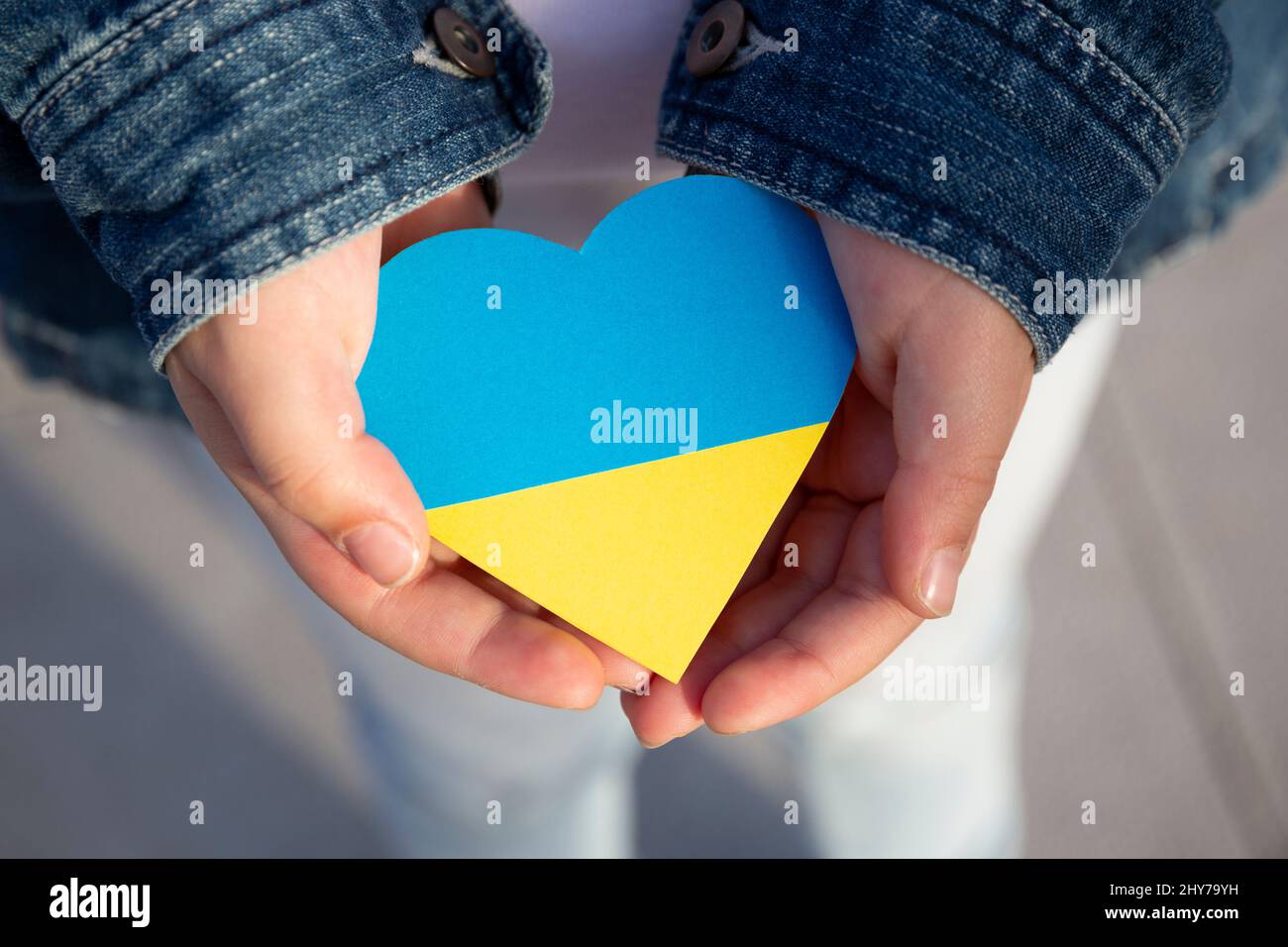 Primo piano delle mani di un bambino piccolo che tiene un cuore nei colori della bandiera Ucraina mostrando sostegno e solidarietà. Protesta contro l'invasione russa Foto Stock