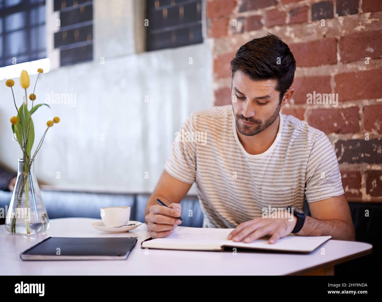 Il materiale di scrittura. Scatto di un bel giovane uomo che scrive in un taccuino mentre si siede ad un tavolo del ristorante. Foto Stock