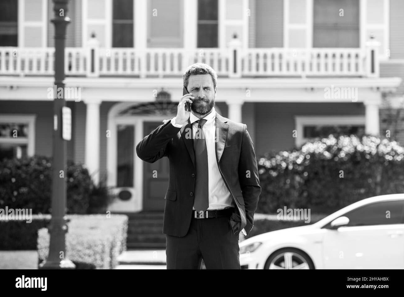 Uomo d'affari che tiene il telefono cellulare usando l'applicazione che invia il messaggio sms che indossa la tuta. Giovane uomo urbano professionale che usa lo smartphone a casa. Immobiliare Foto Stock