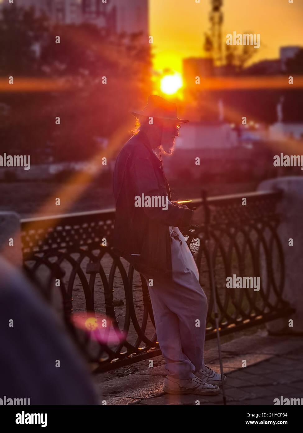 Colpo verticale di un vecchio uomo con un cappello a Ekaterinburg da Iset recinzione del fiume con raggi del tramonto Foto Stock