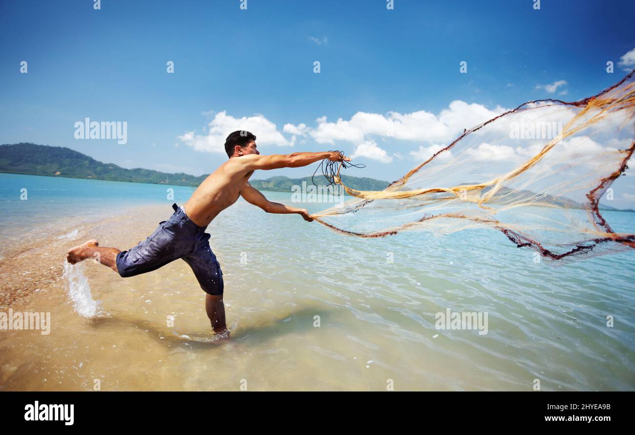 Gettando le sue reti. Shot di un tradizionale pescatore tailandese in piedi in acqua gettando una rete nell'oceano. Foto Stock