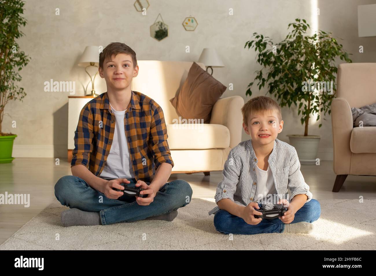 Ritratto di due ragazzi si siede sul pavimento in una stanza che gioca video giochi con joystick Foto Stock