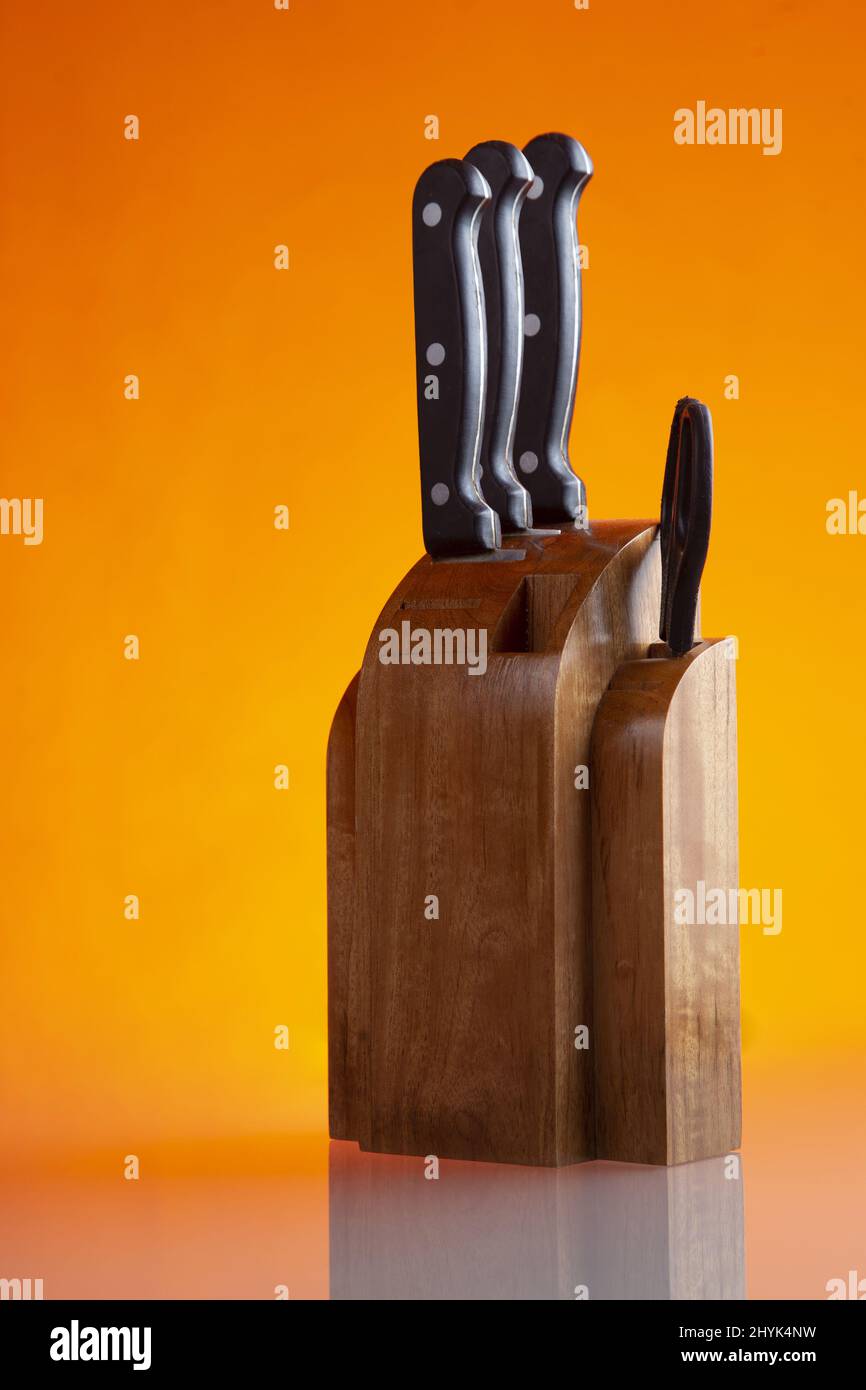Primo piano verticale di una serie di coltelli da cucina isolati su sfondo arancione Foto Stock