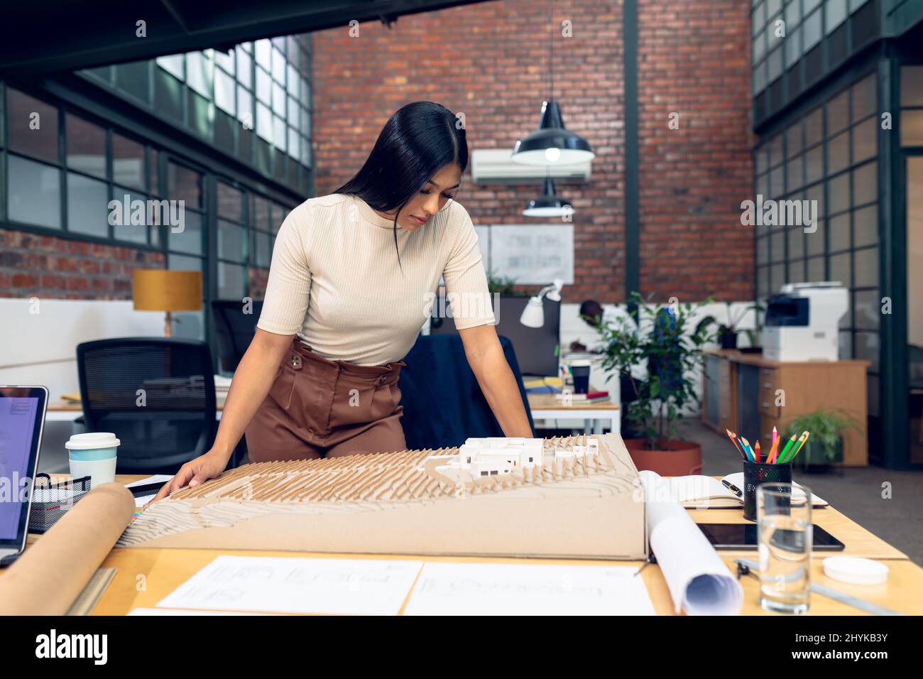 Giovane architetto biraciale che analizza il modello di costruzione alla scrivania in un ufficio moderno Foto Stock